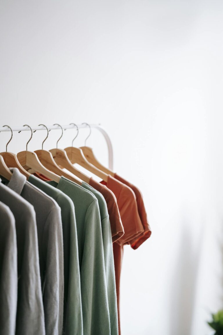 Light room interior with collection of various garments on wooden racks in wardrobe near white walls