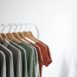 Light room interior with collection of various garments on wooden racks in wardrobe near white walls